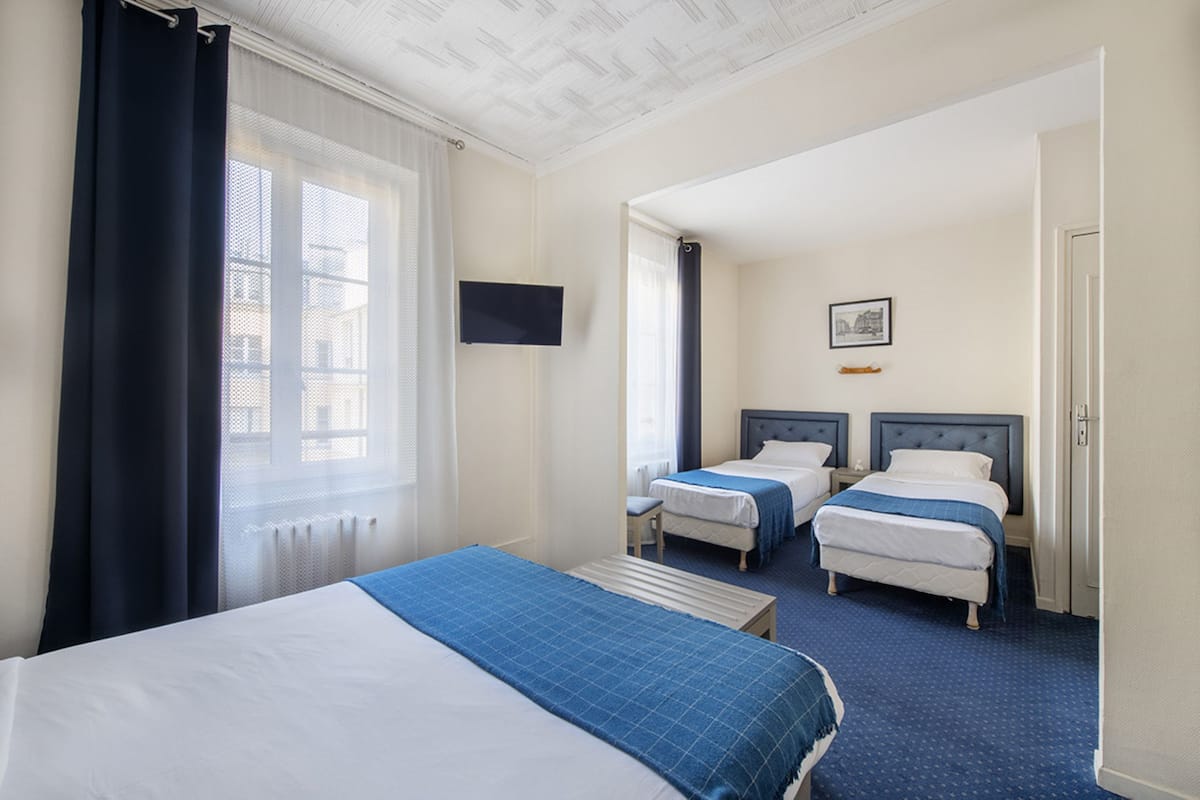 A hotel room with two beds, a television, a picture on the wall, and a window with curtains.