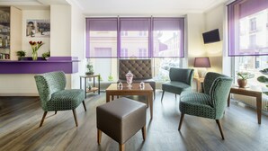 A modern hotel lobby with a seating area, a reception desk, and a large window with a view of buildings. - Royal Hôtel (Versailles)