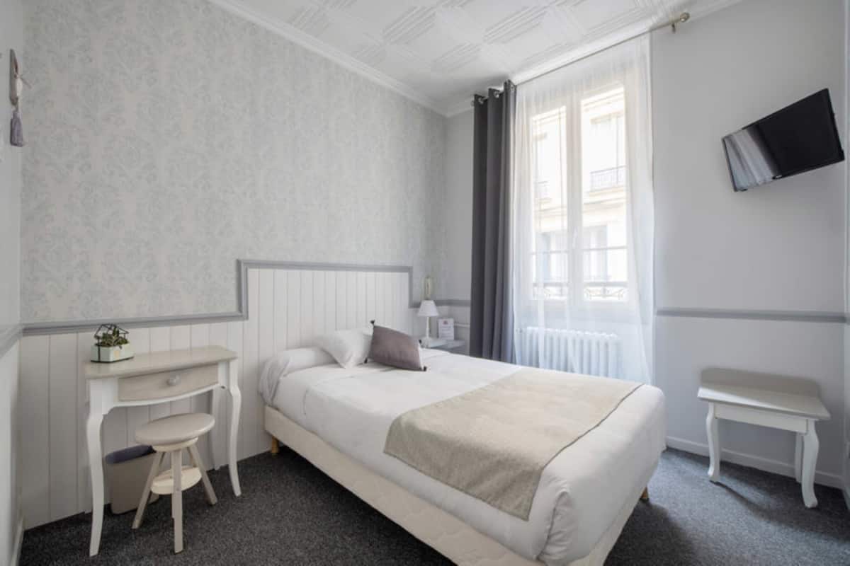 A hotel room with a bed, a desk, a chair, a TV, and a window with curtains.