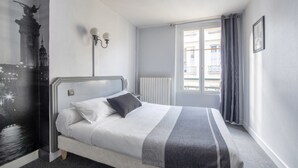 A bedroom with a bed, a radiator, a window with curtains, and a wall-mounted light fixture. - Royal Hôtel (Versailles)