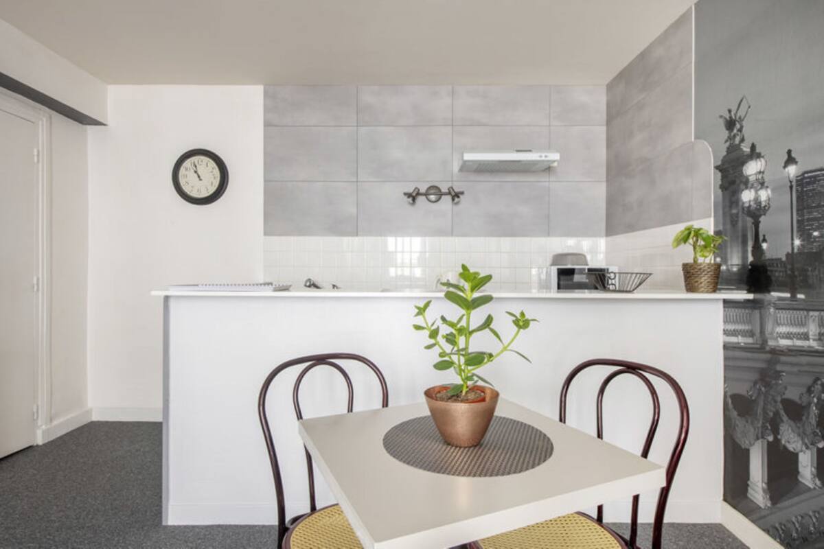 A modern kitchen with a white countertop, two chairs, a clock, and a potted plant.