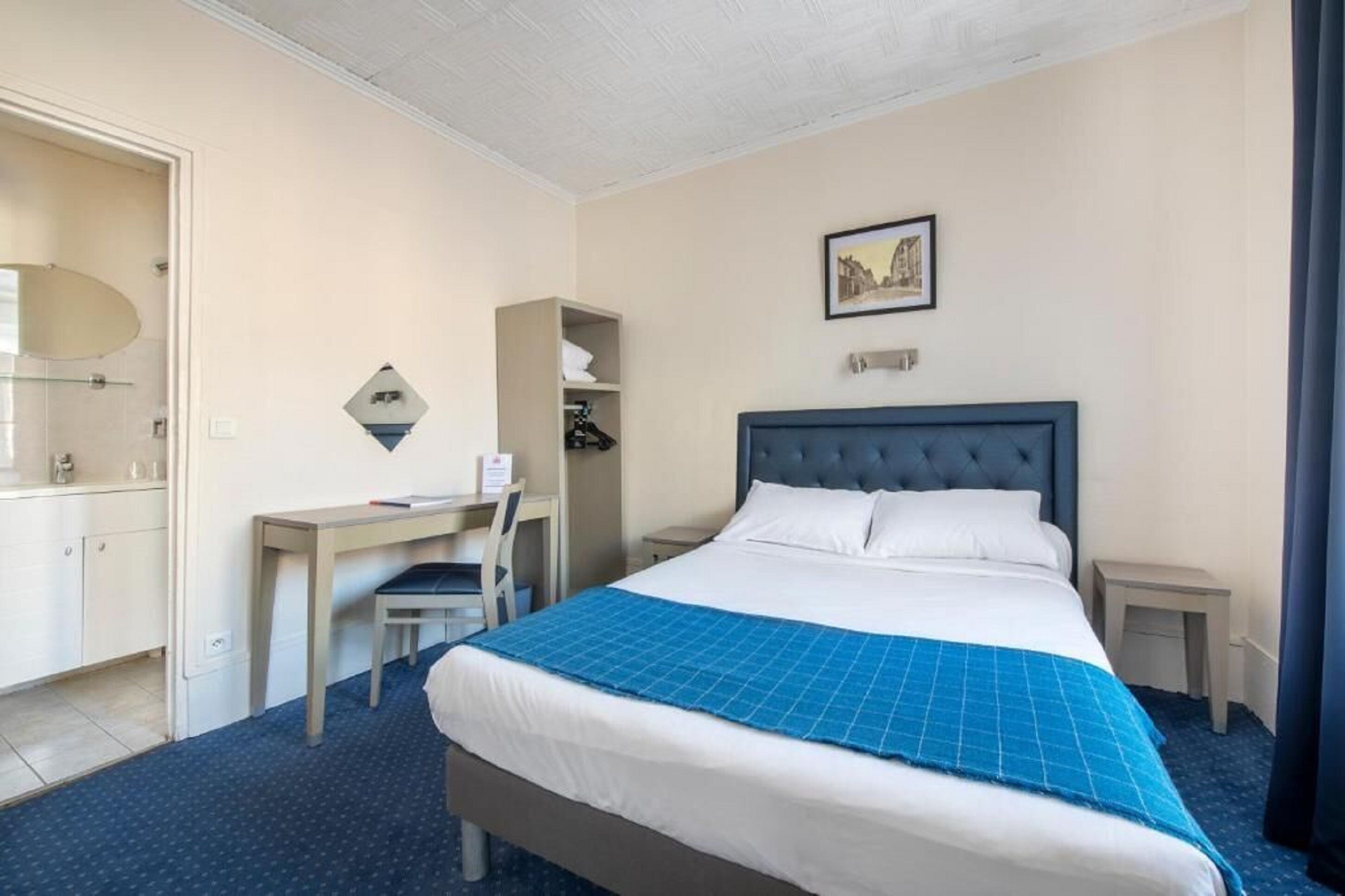 Een hotelkamer met een groot bed, een bureau, een stoel, een kledingkast en een schilderij aan de muur.