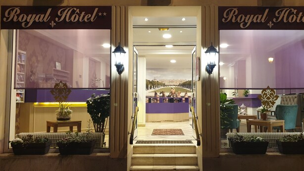 The entrance of the Royal Hotel with a reception desk, potted plants, and a view of the interior. - Royal Hôtel (Versailles)