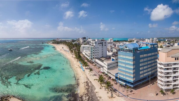 Eine Küstenstadt mit Strand, klarem türkisblauem Wasser und einem markanten, blauen Hotelgebäude.