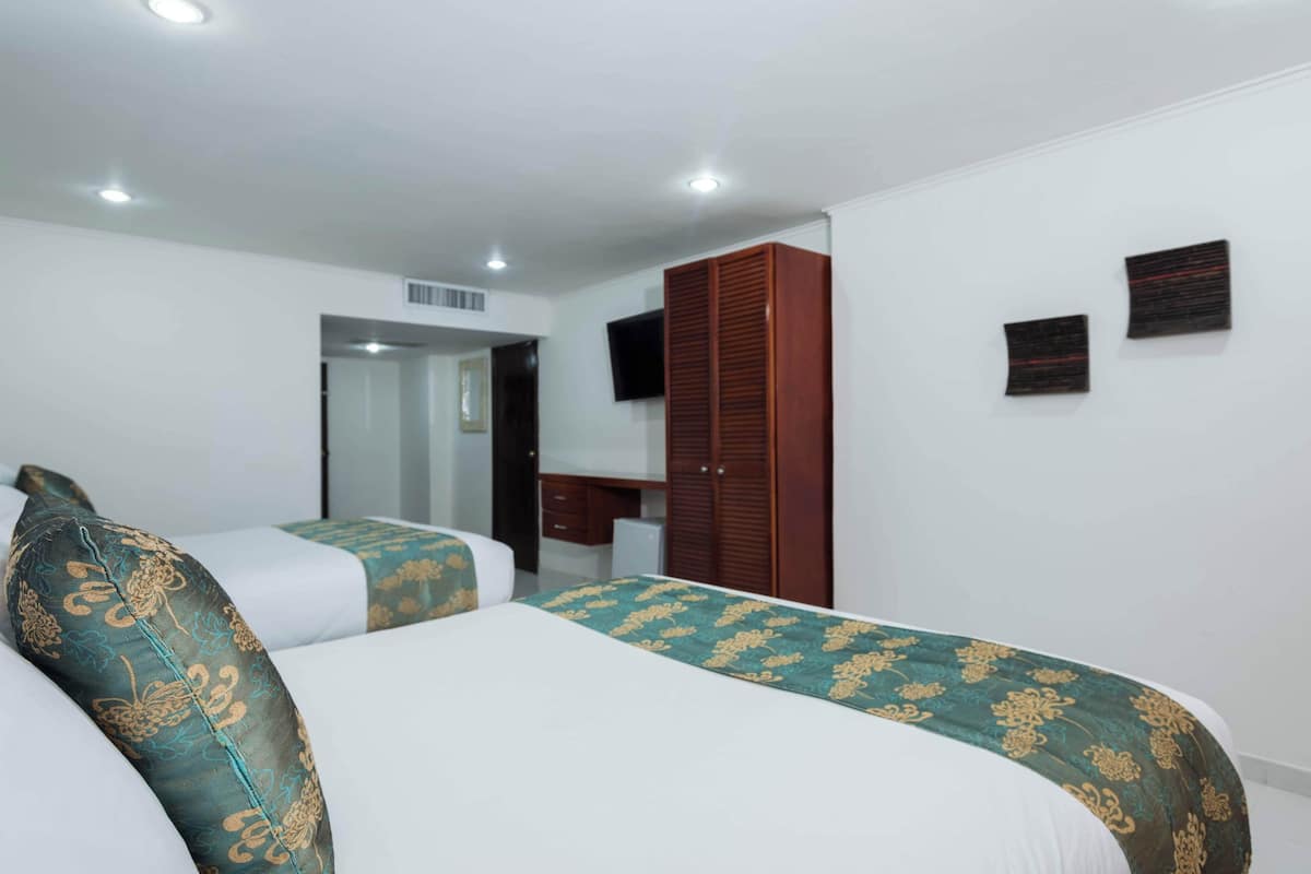 A hotel room with two beds, a wooden wardrobe, a desk, and a television on the wall.