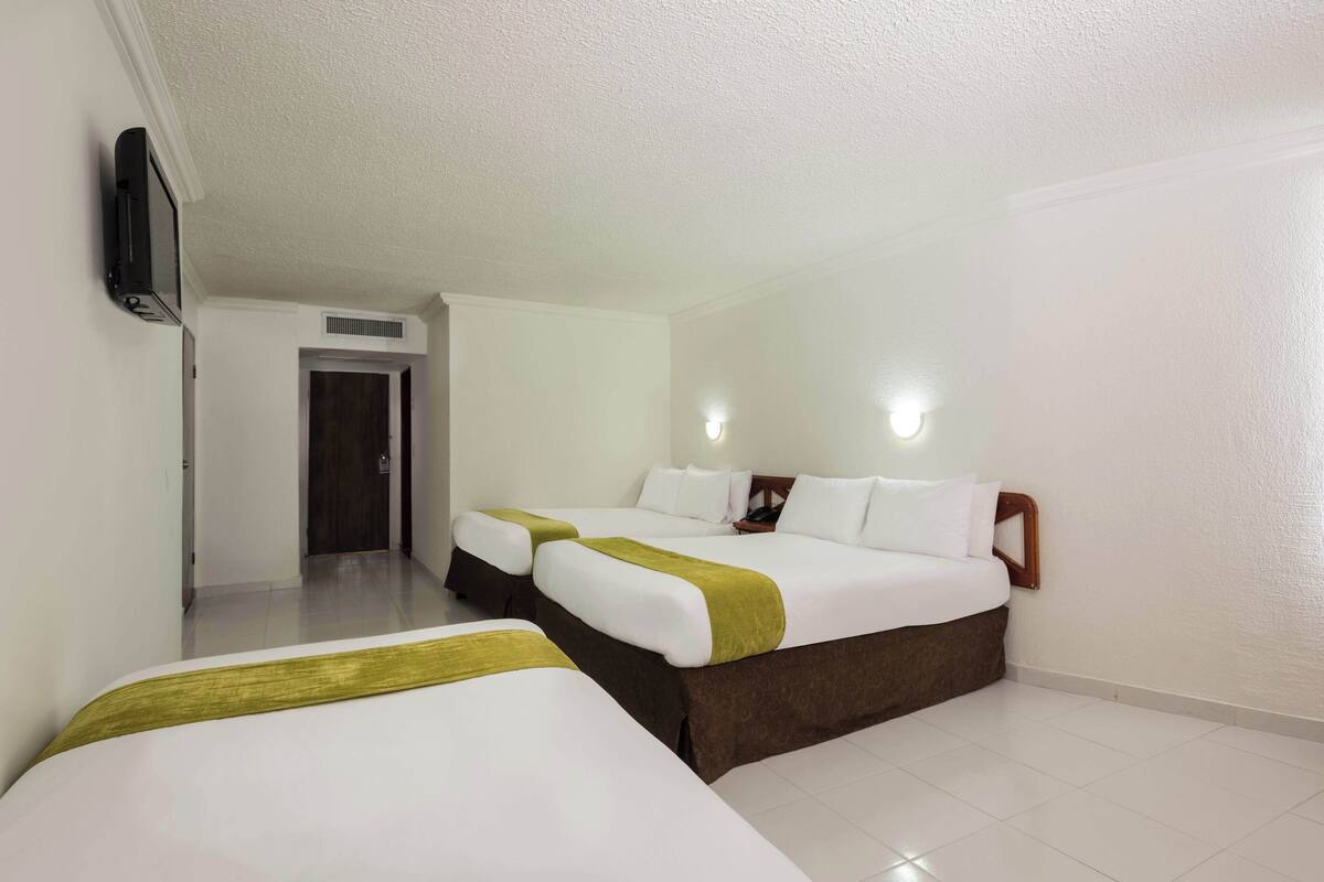 A hotel room with two beds, a television mounted on the wall, and a door leading to another room.