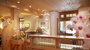 A wooden interior with a glass railing, wooden columns, and a flower arrangement. - Hotel Casanna (Davos)