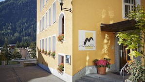A hotel with a yellow facade, a signboard, and a mountain backdrop. - Hotel Casanna (Davos)