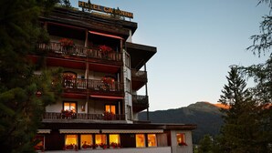 A multi-story hotel with balconies adorned with flowers, a sign reading "Hotel Caronna," and a mountainous backdrop. - Hotel Casanna (Davos)
