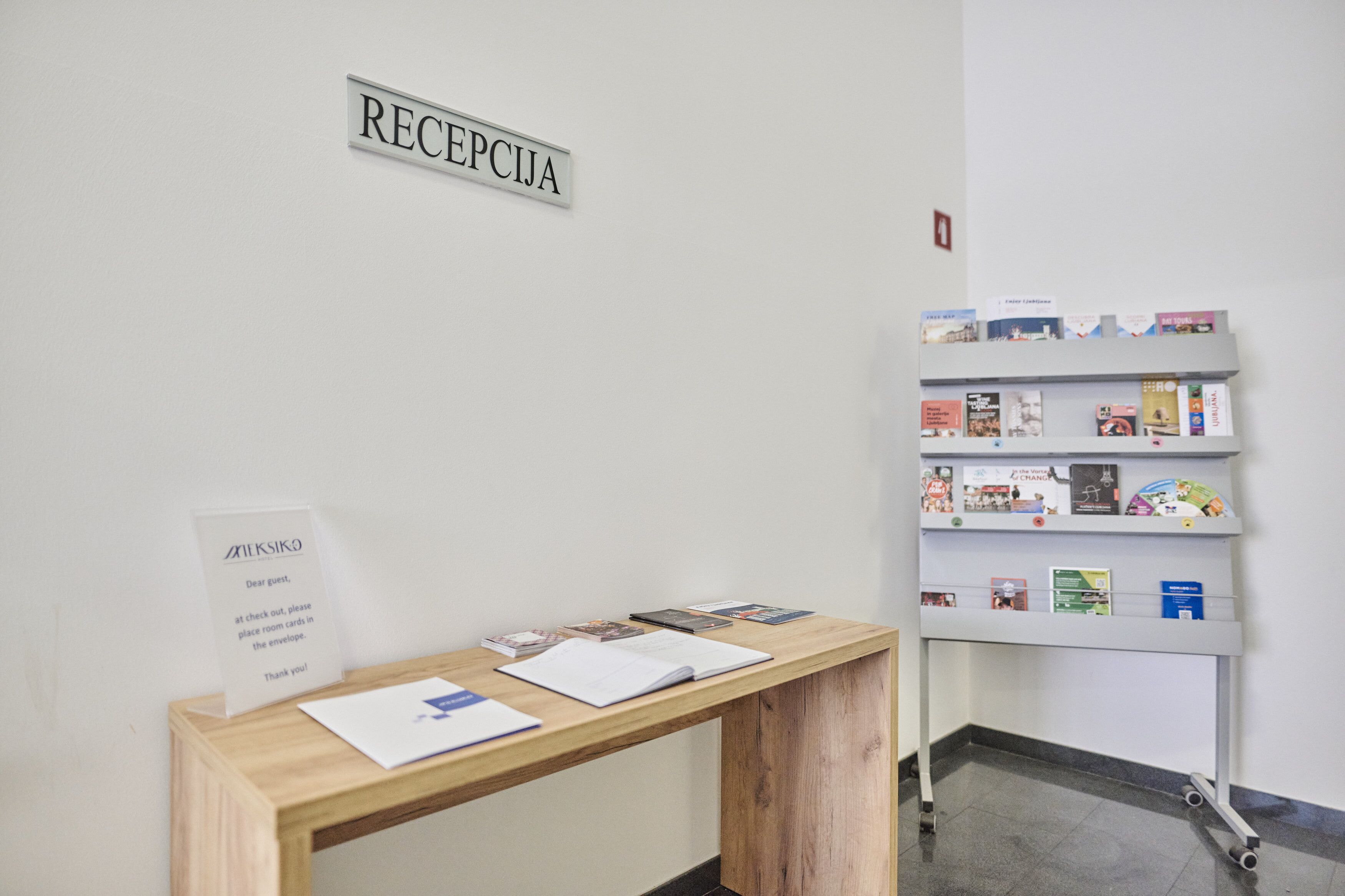 Un comptoir d’accueil avec une enseigne au-dessus, une table en bois avec des documents et une bibliothèque contenant divers livres et brochures.
