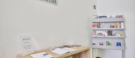 Un comptoir d’accueil avec une enseigne au-dessus, une table en bois avec des documents et une bibliothèque contenant divers livres et brochures.