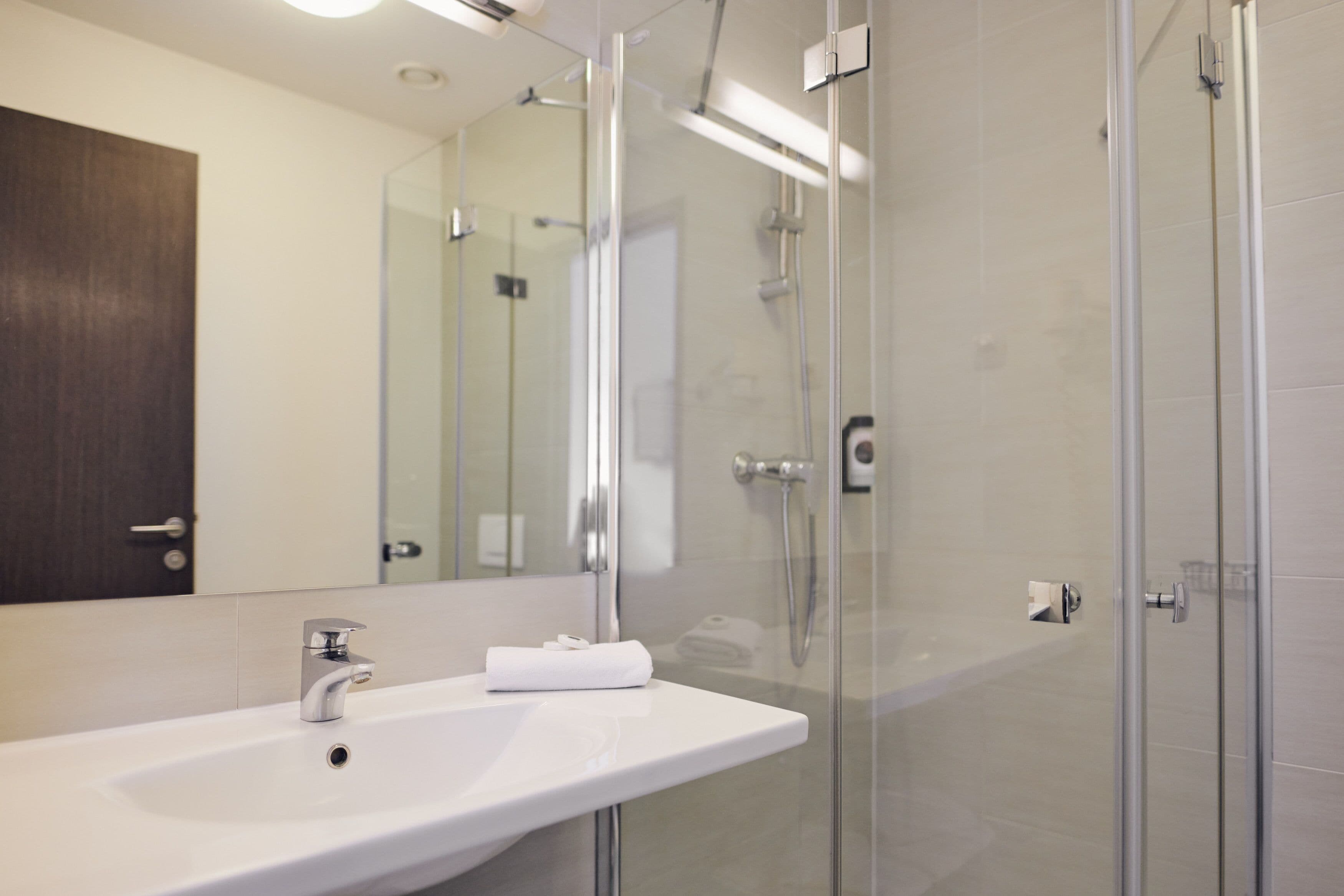 A modern bathroom with a white sink, a glass shower enclosure, and a large mirror.