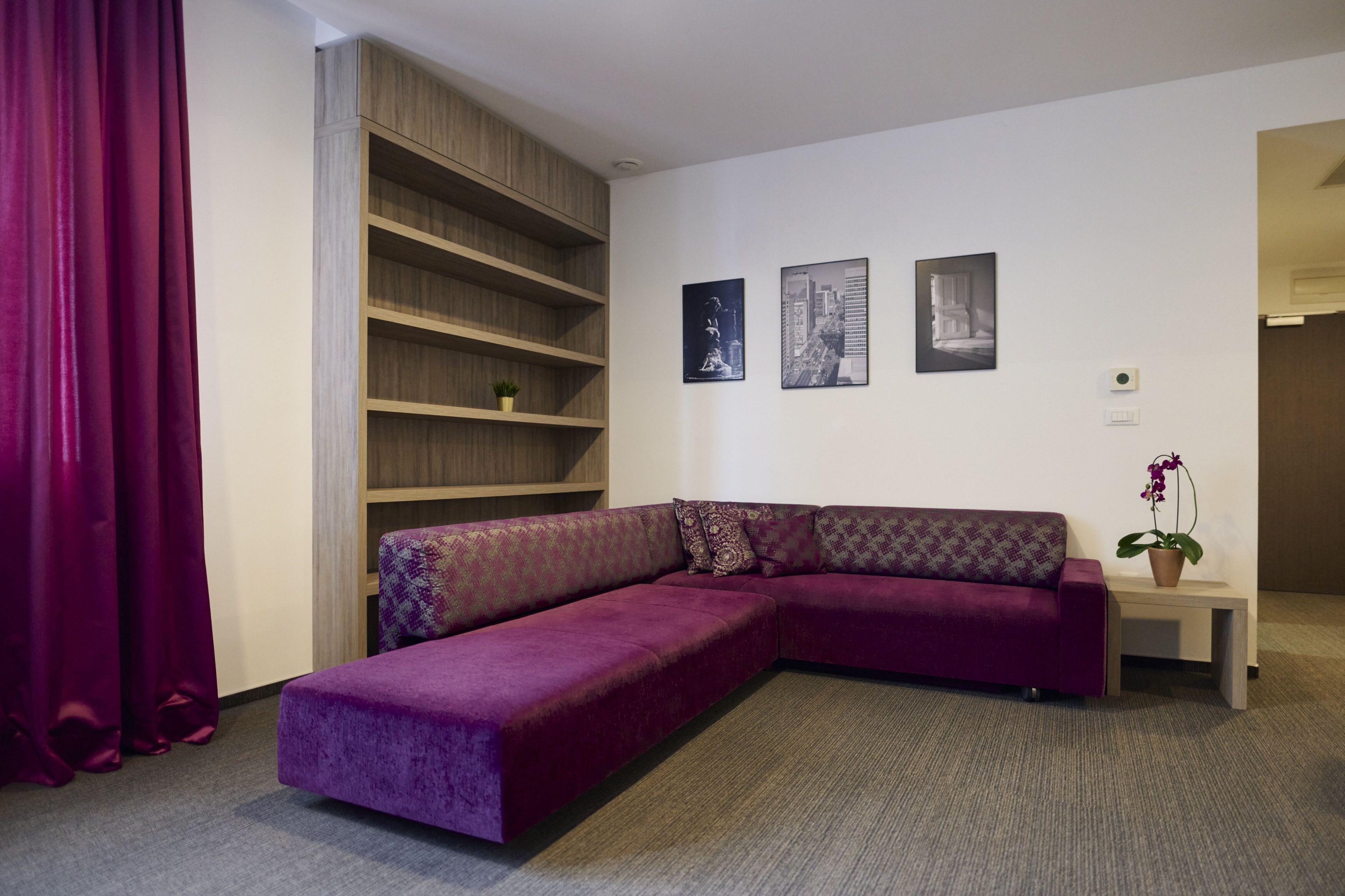 A modern living room with a purple sectional sofa, a wooden shelving unit, and three framed pictures on the wall.