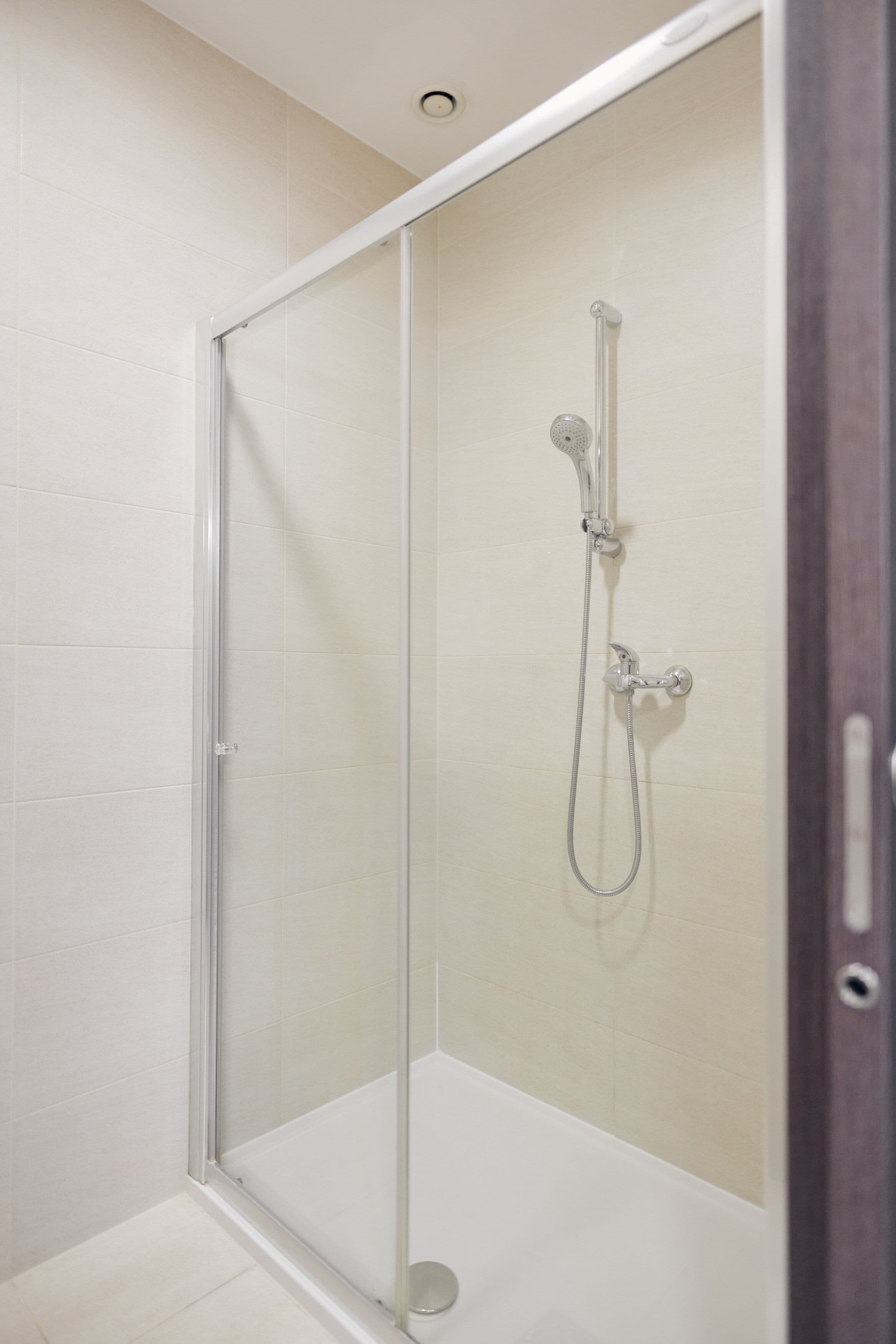 A glass-enclosed shower stall with a handheld showerhead and a wall-mounted faucet.