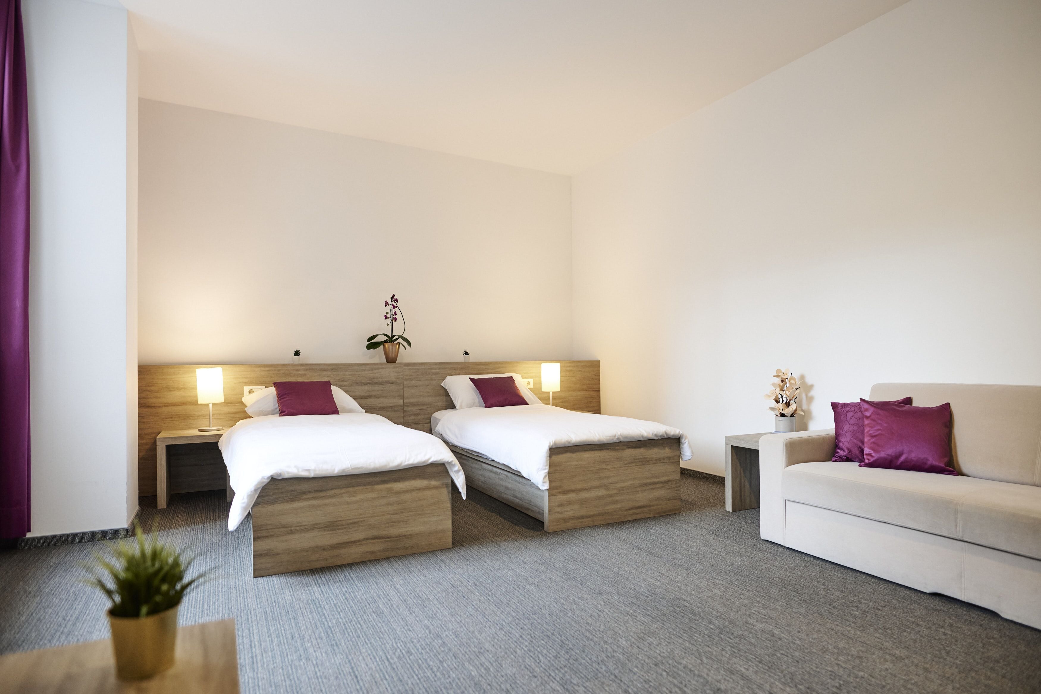 Een hotelkamer met twee bedden, een bank, een nachtkastje en een kleine tafel met een plant.