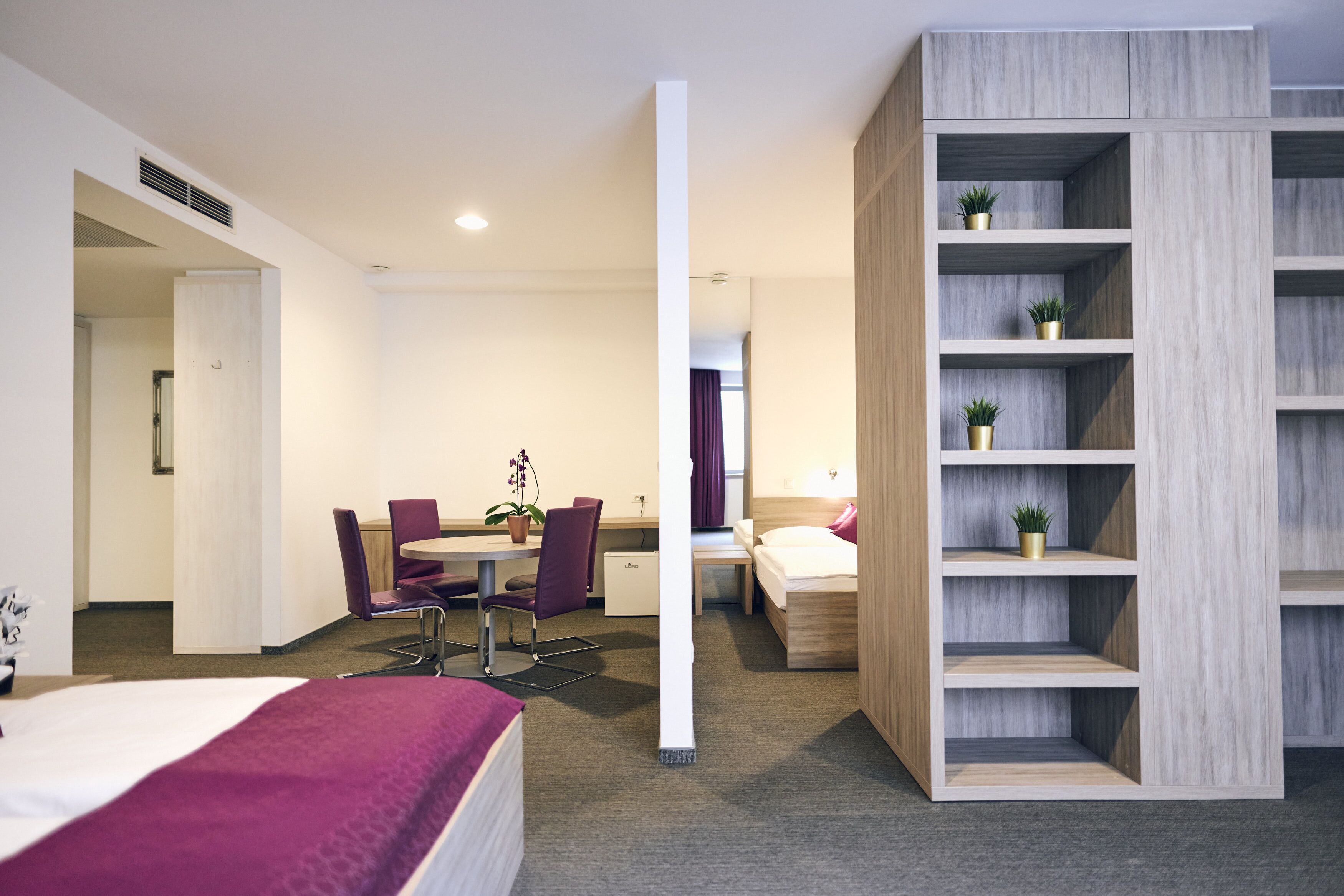 Una habitación de hotel con cama, escritorio, silla, una mesita y estantería.