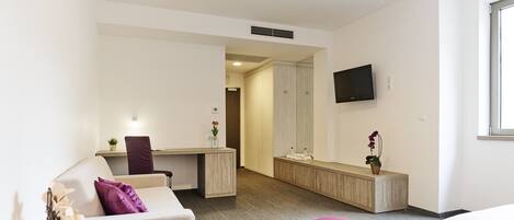 A hotel room with a bed, a desk, a chair, a TV, and a bathroom visible through an open door.