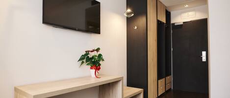 Una recepción moderna con una consola de madera, una planta en maceta, un televisor de pantalla plana y una puerta de tonos oscuros.