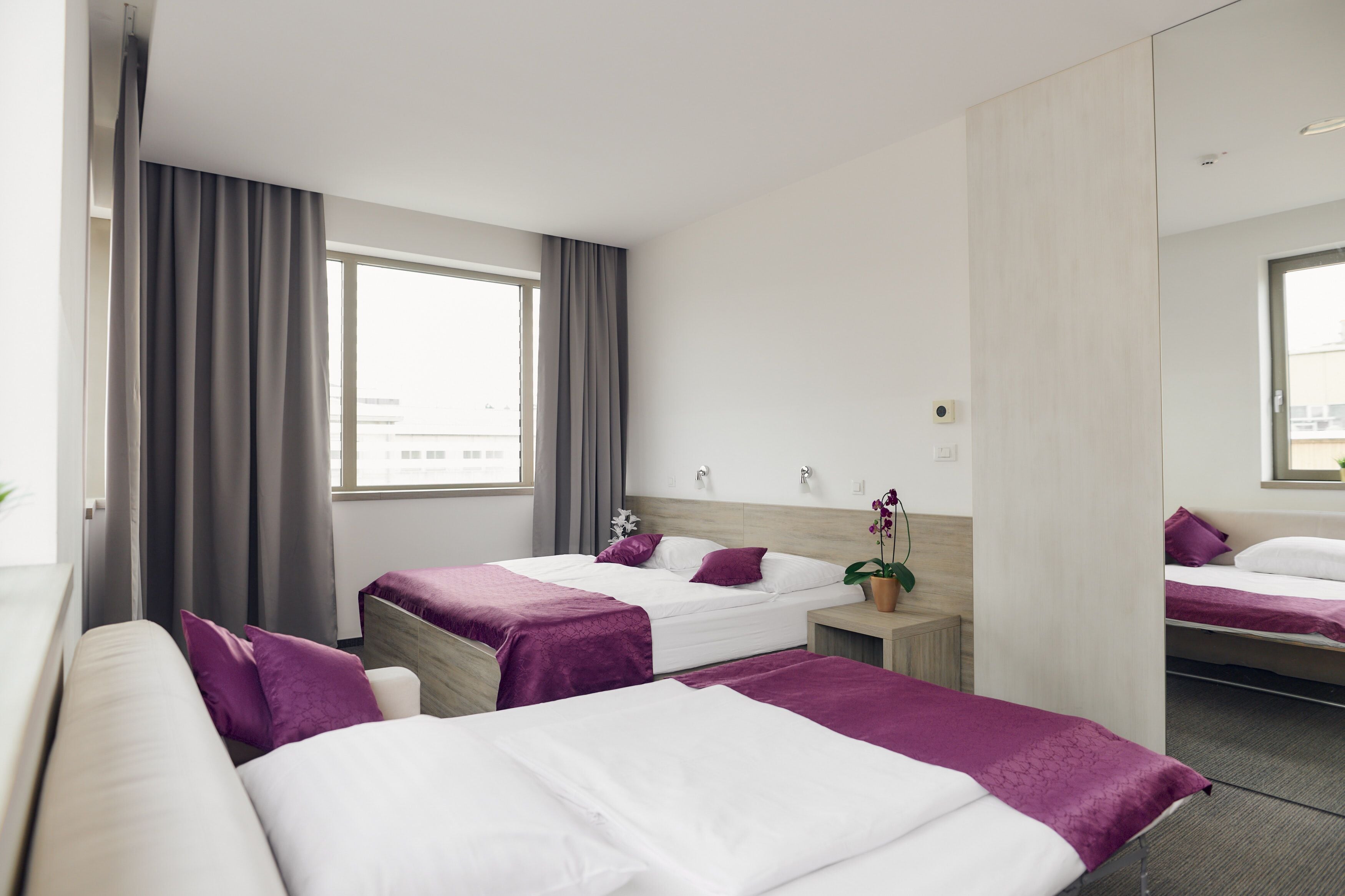 Een hotelkamer met twee bedden, een bank, een nachtkastje, een spiegel en een raam met gordijnen.