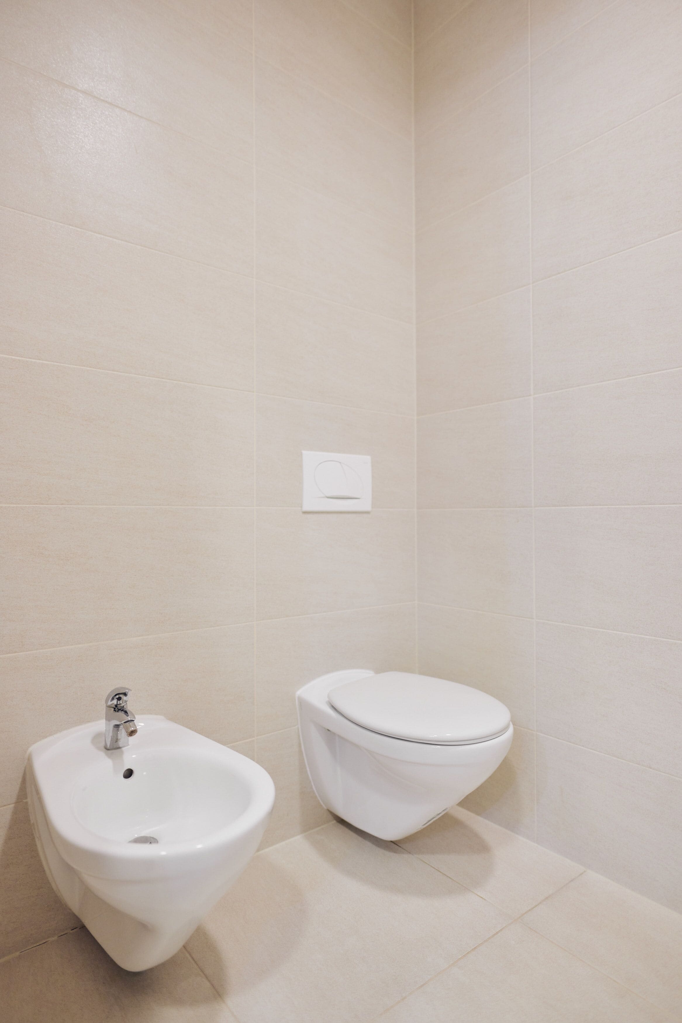 Une salle de bain équipée d’un bidet, de toilettes et d’une commande de chasse d’eau fixée au mur.