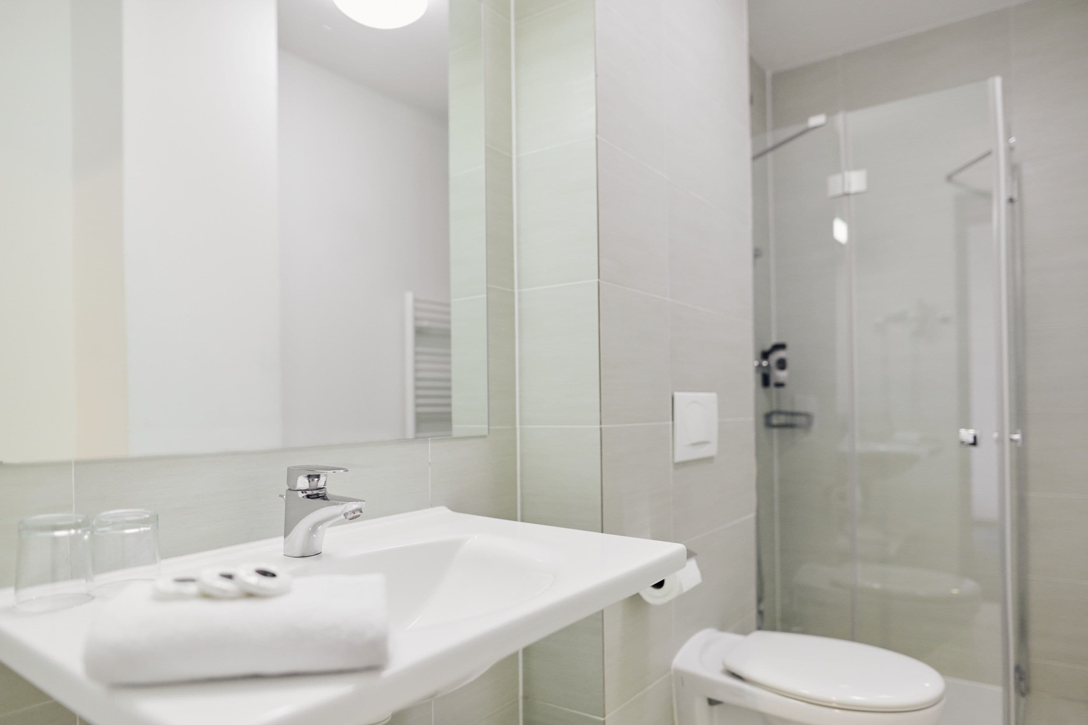 A modern bathroom with a white sink, mirror, and glass shower enclosure.