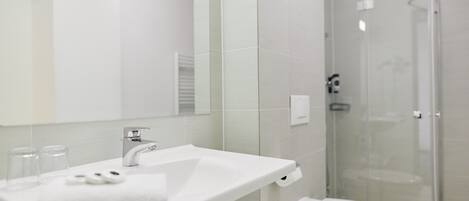 A modern bathroom with a white sink, mirror, and glass shower enclosure.