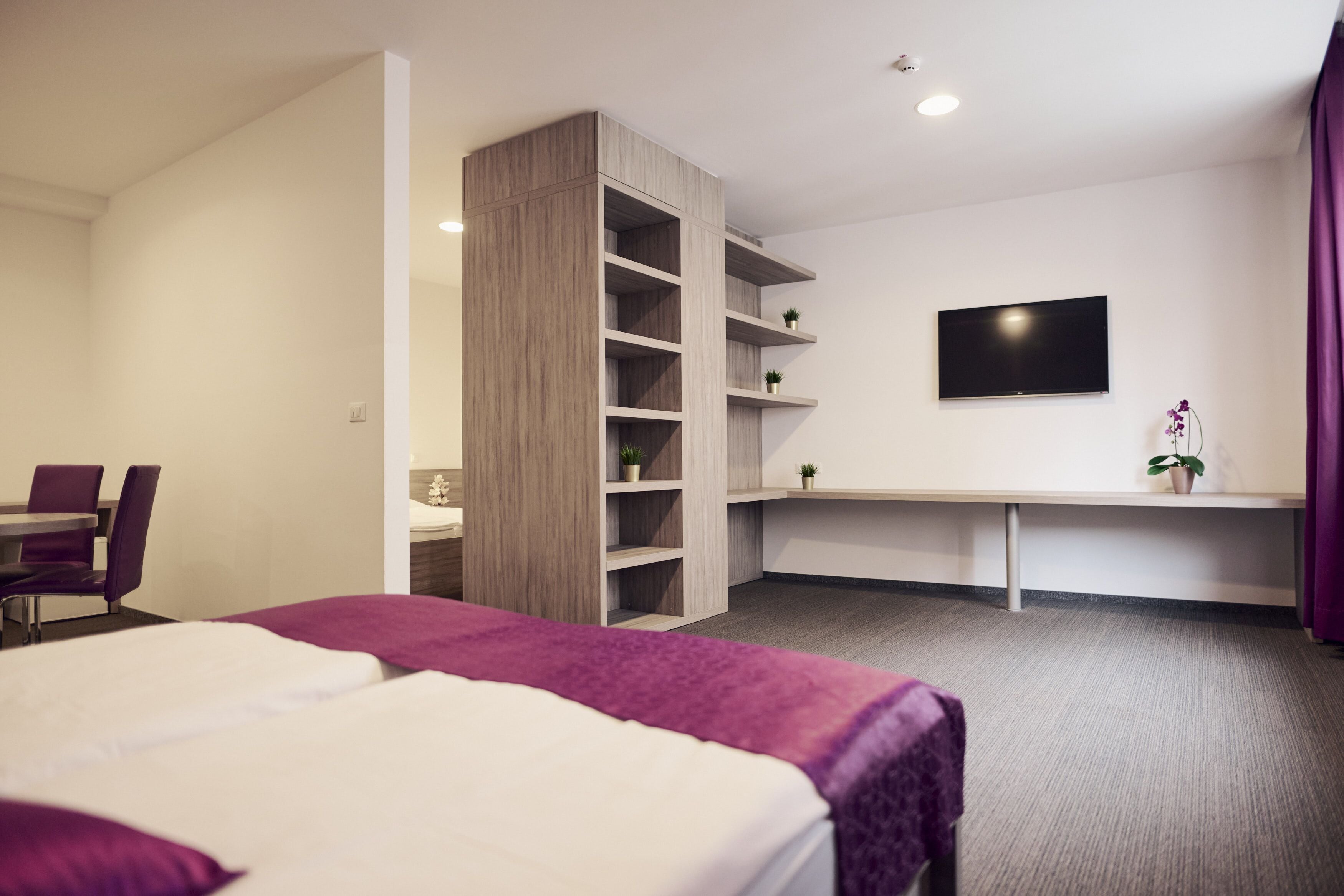 Een hotelkamer met een bed, een bureau, een televisie en een plank.