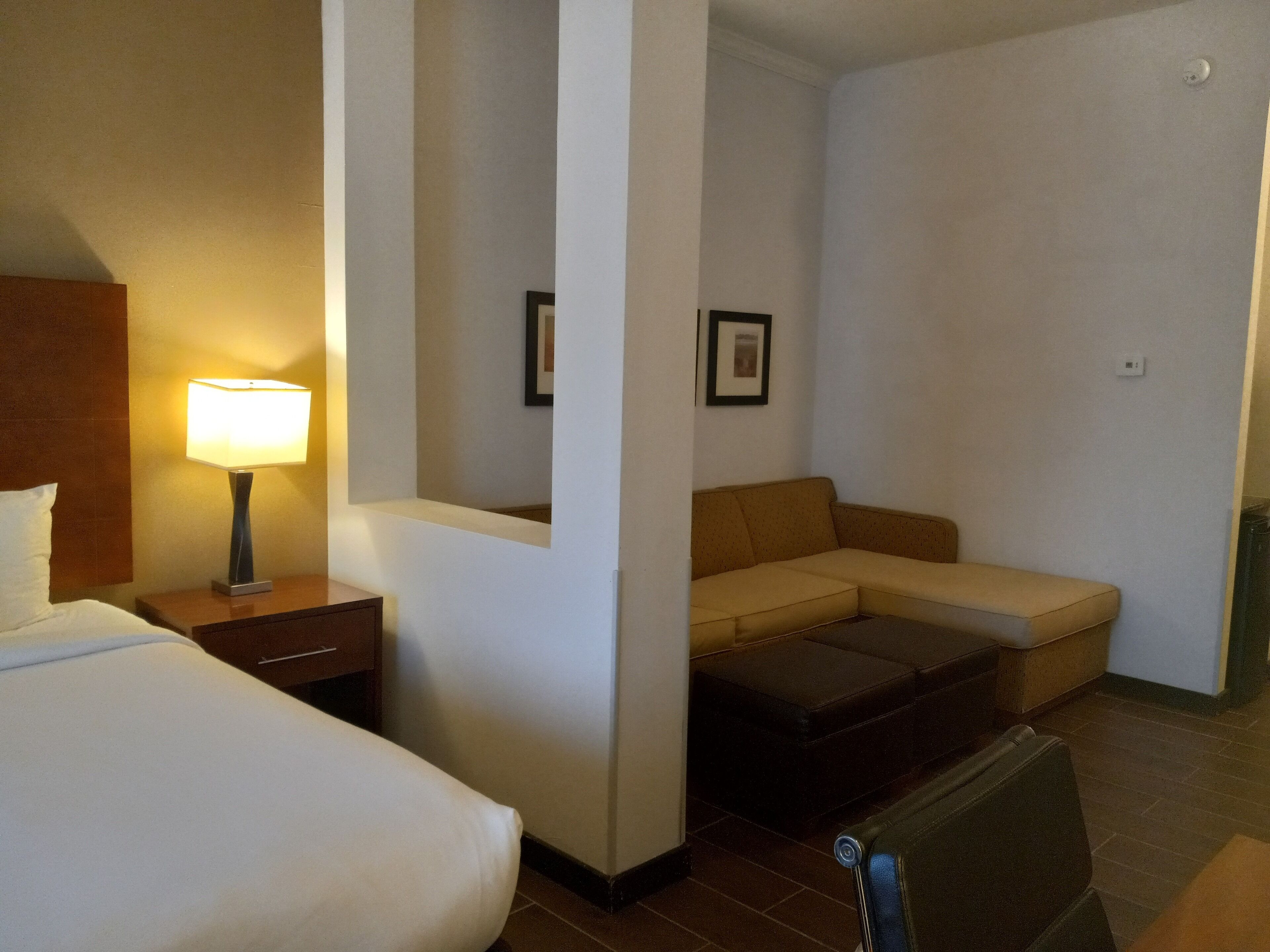 A hotel room with a bed, a nightstand with a lamp, a sofa, and a small table.