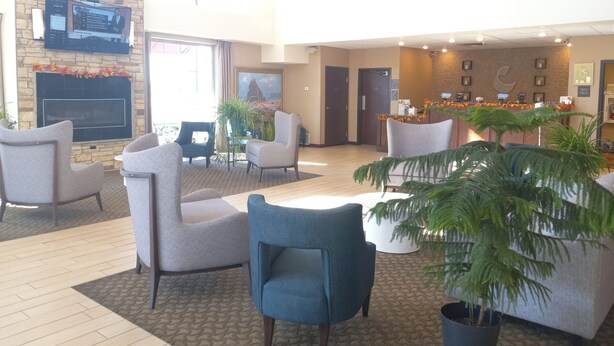 A spacious lobby with a stone fireplace, comfortable seating, a reception desk, and a large painting on the wall. - Comfort Suites Farmington (Farmington)