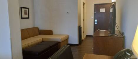 A hotel room with a sofa, a small table, a desk with a telephone, and a television.