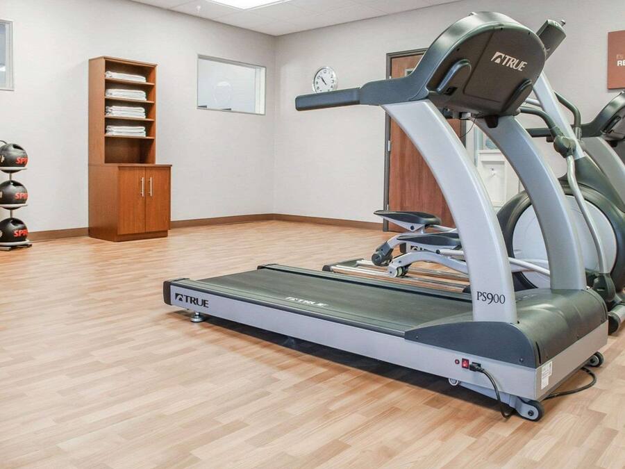A gym with a treadmill, a wooden cabinet, and a wall clock.