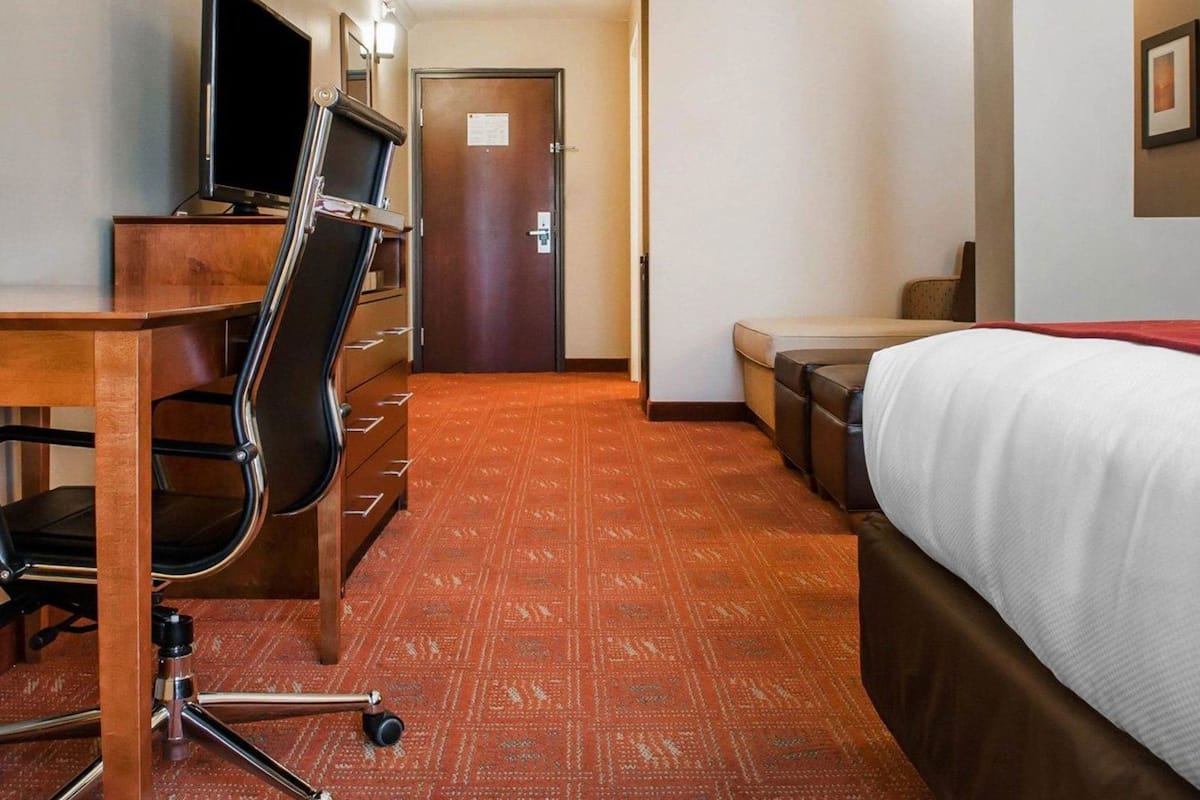 Ein Hotelzimmer mit Bett, Schreibtisch, Stuhl, Fernseher und einer Tür.