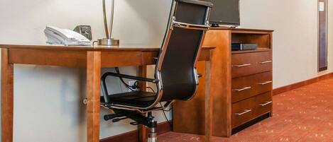 A hotel workspace with a desk, chair, lamp, phone, and TV.