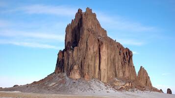 A large, rugged rock formation with a flat base and steep sides, set against a clear blue sky.