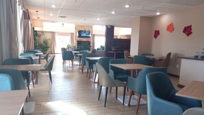 A spacious restaurant with multiple tables and chairs, a television mounted on the wall, and a few decorative leaves on the wall. - Comfort Suites Farmington (Farmington)