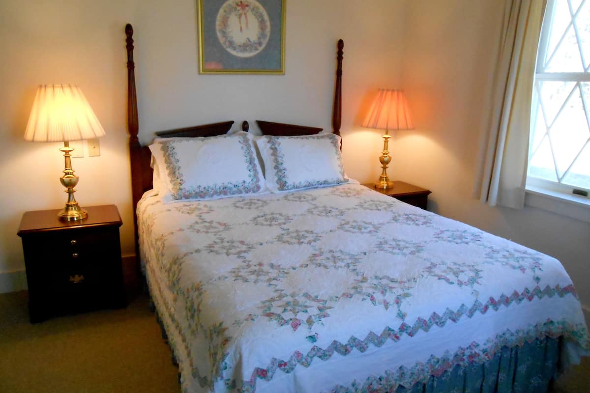 A neatly made bed with floral bedding, two bedside lamps, a nightstand, and a framed picture on the wall.