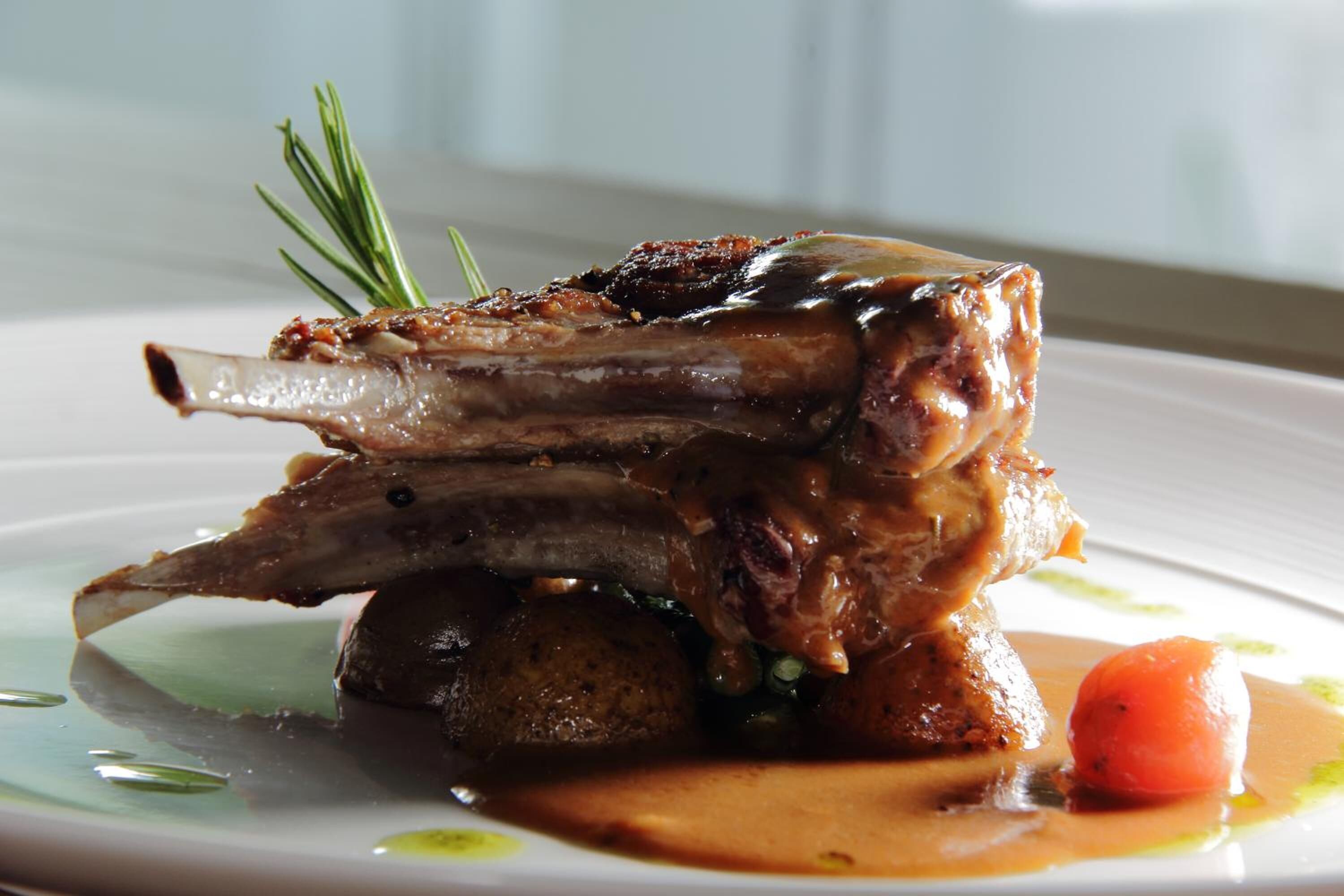 A plate with a lamb shank, vegetables, and a sauce.