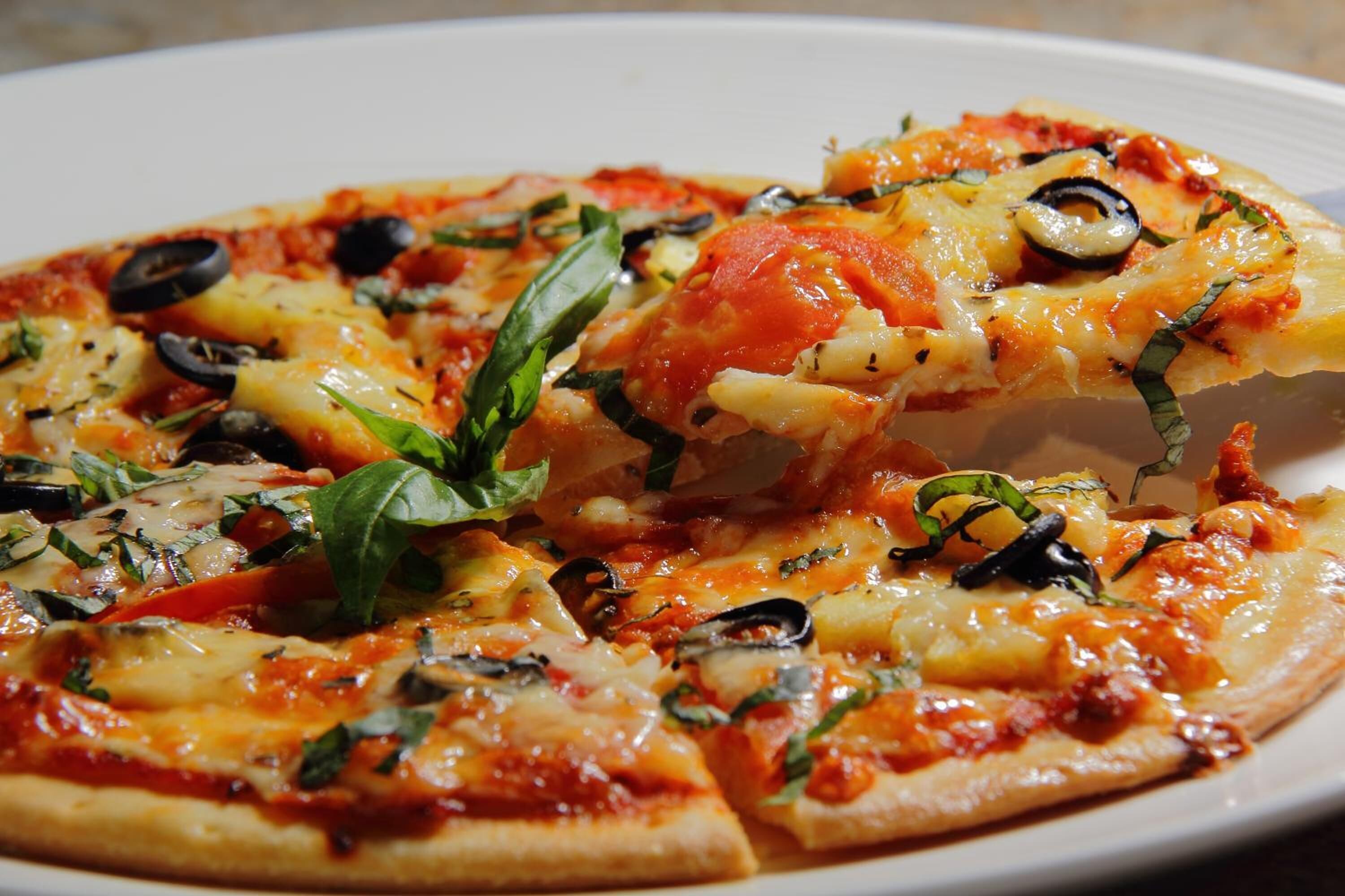 A pizza with toppings like olives, tomatoes, and basil on a white plate.