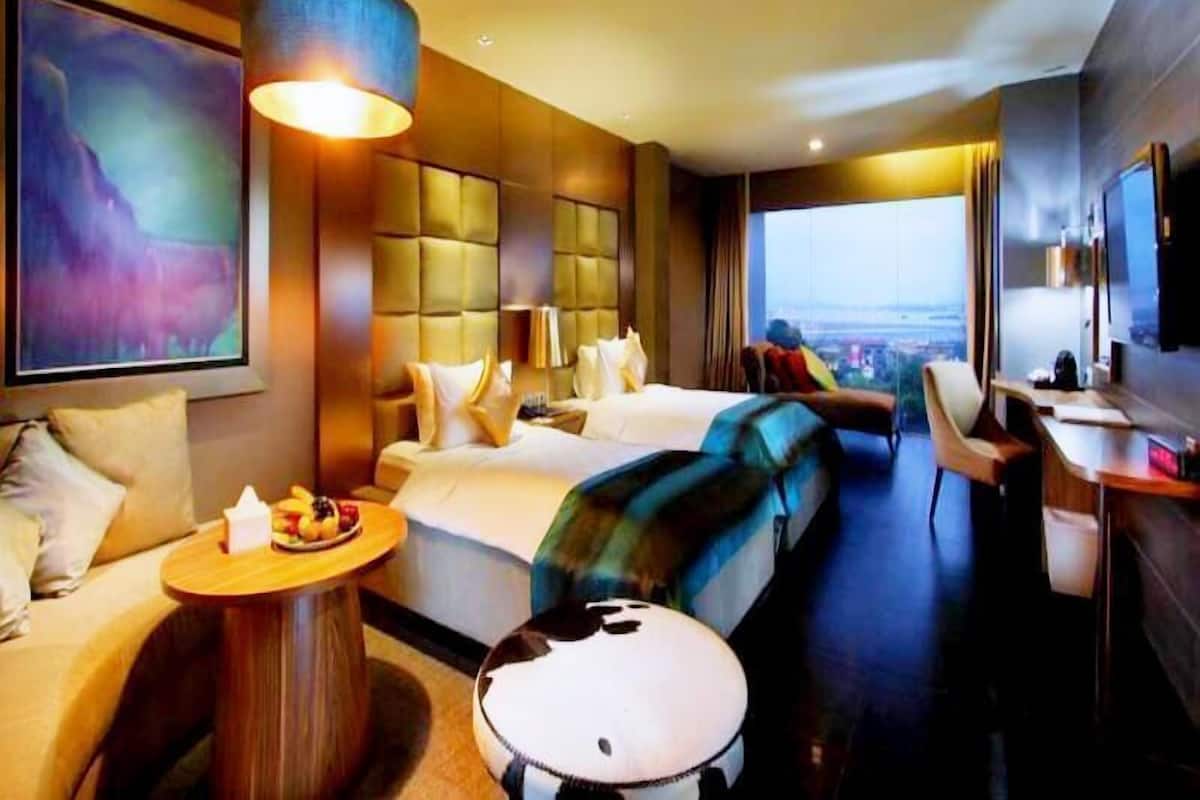 Moderni hotellihuone, jossa on suuri sänky, sohva, työpöytä ja näkymä kaupunkiin.