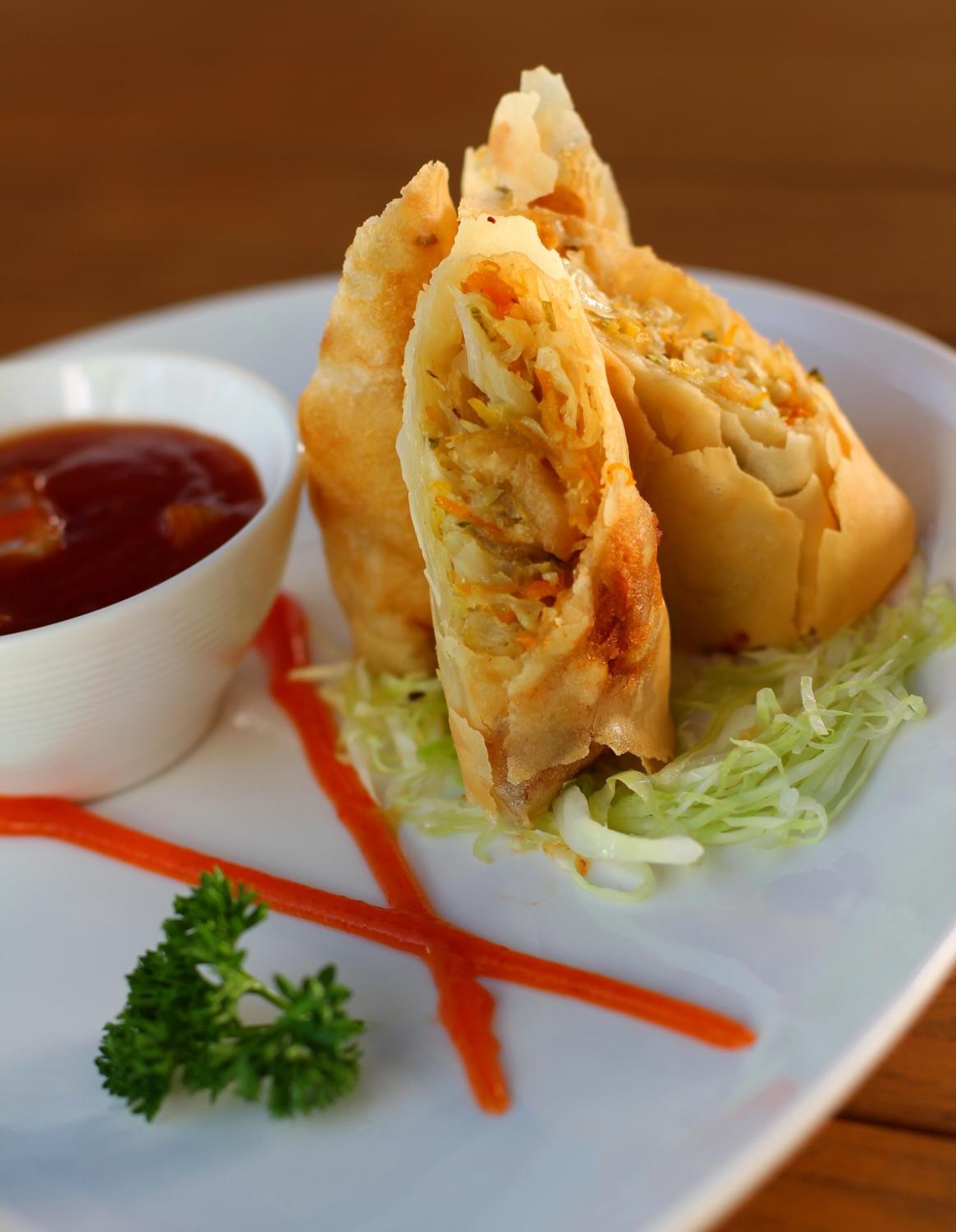 A plate with two fried spring rolls, a side of dipping sauce, and a garnish of parsley.