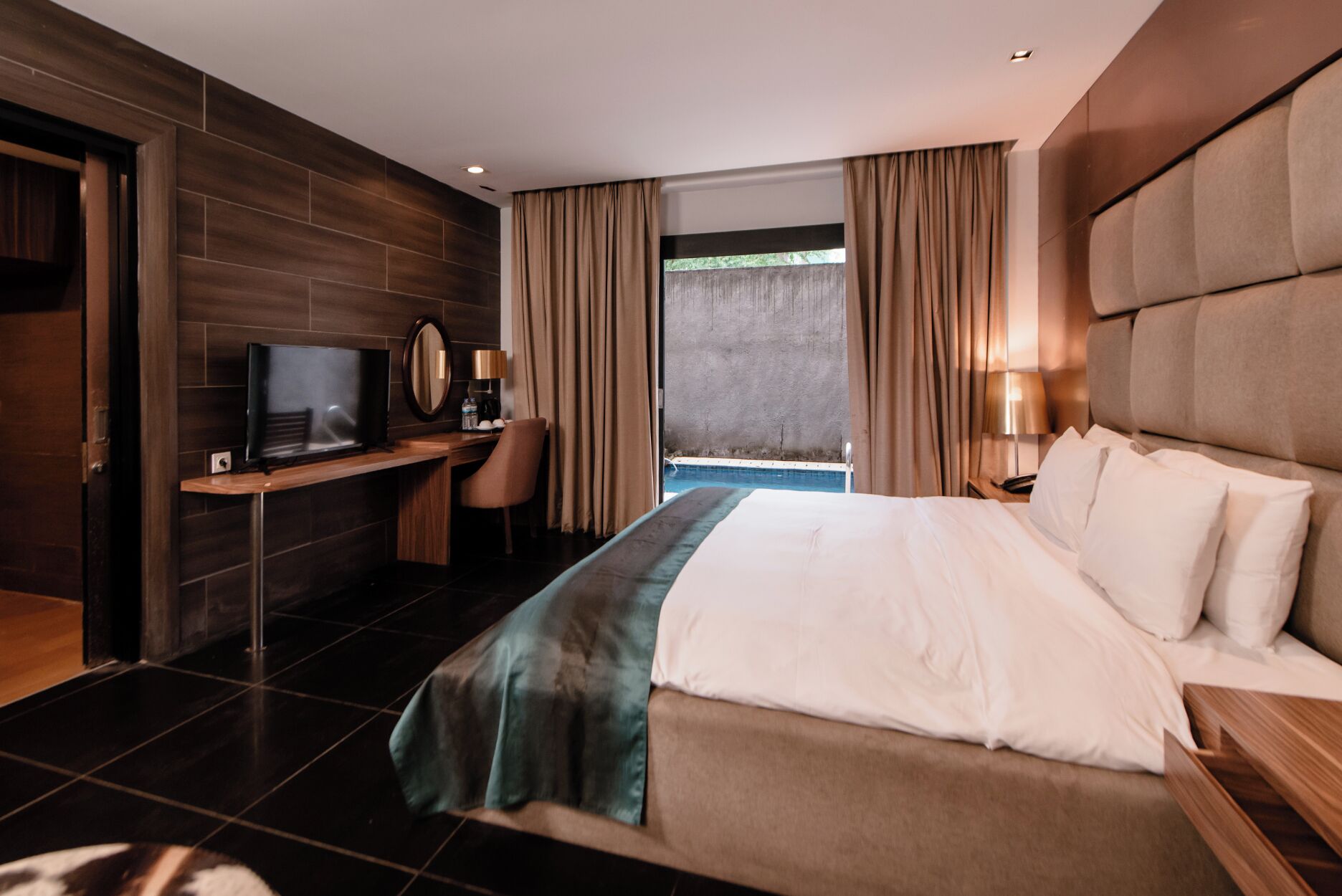 Ein modernes Hotelzimmer mit einem großen Bett, einem Schreibtisch mit Fernseher und Blick ins Freie.