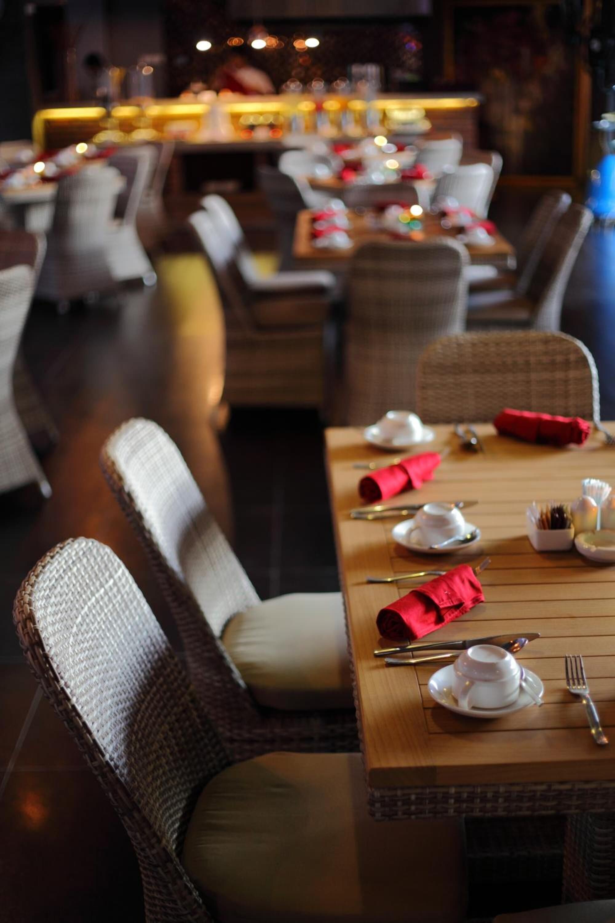 Ein Restaurantambiente mit Korbstühlen und Tischen, gedeckt mit weißen Tellern und roten Servietten.