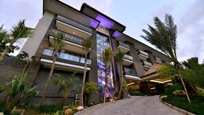 A modern hotel with a prominent entrance, multiple floors, and a well-maintained outdoor area with palm trees and plants.