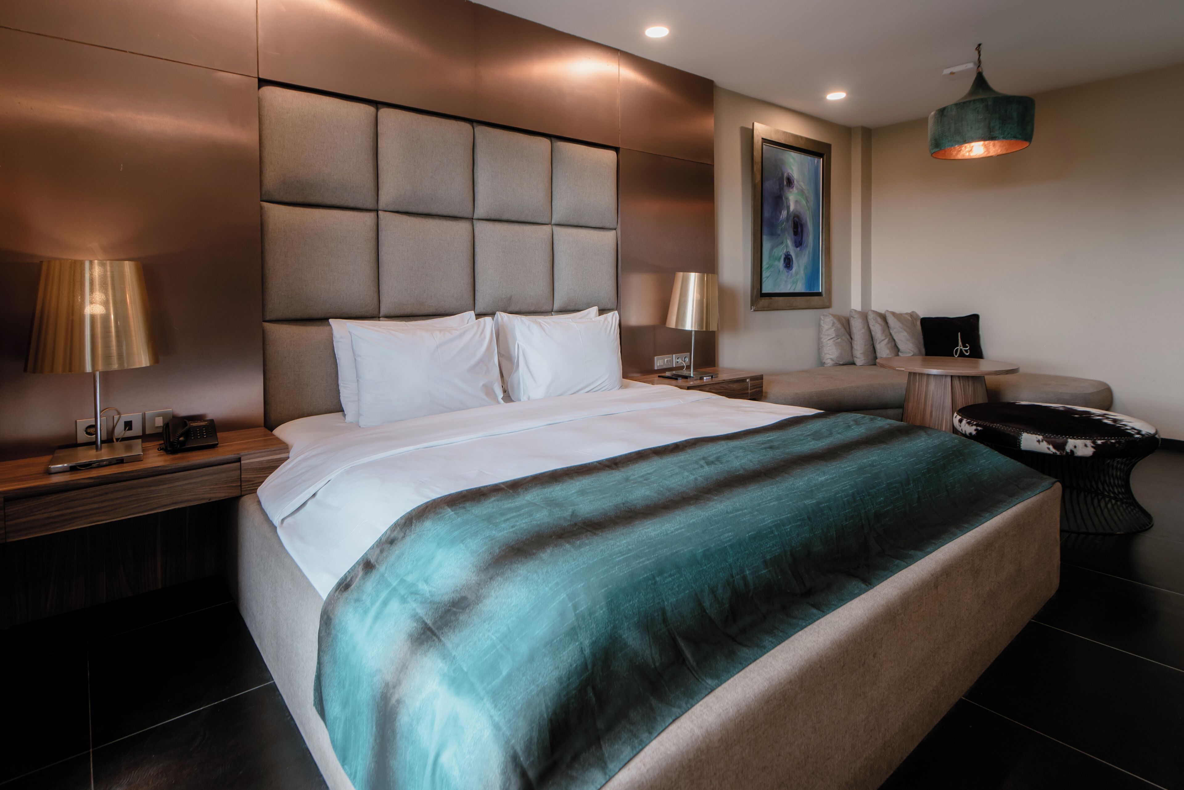 A modern hotel room with a large bed, a sofa, a round coffee table, and a unique wall-mounted light fixture.