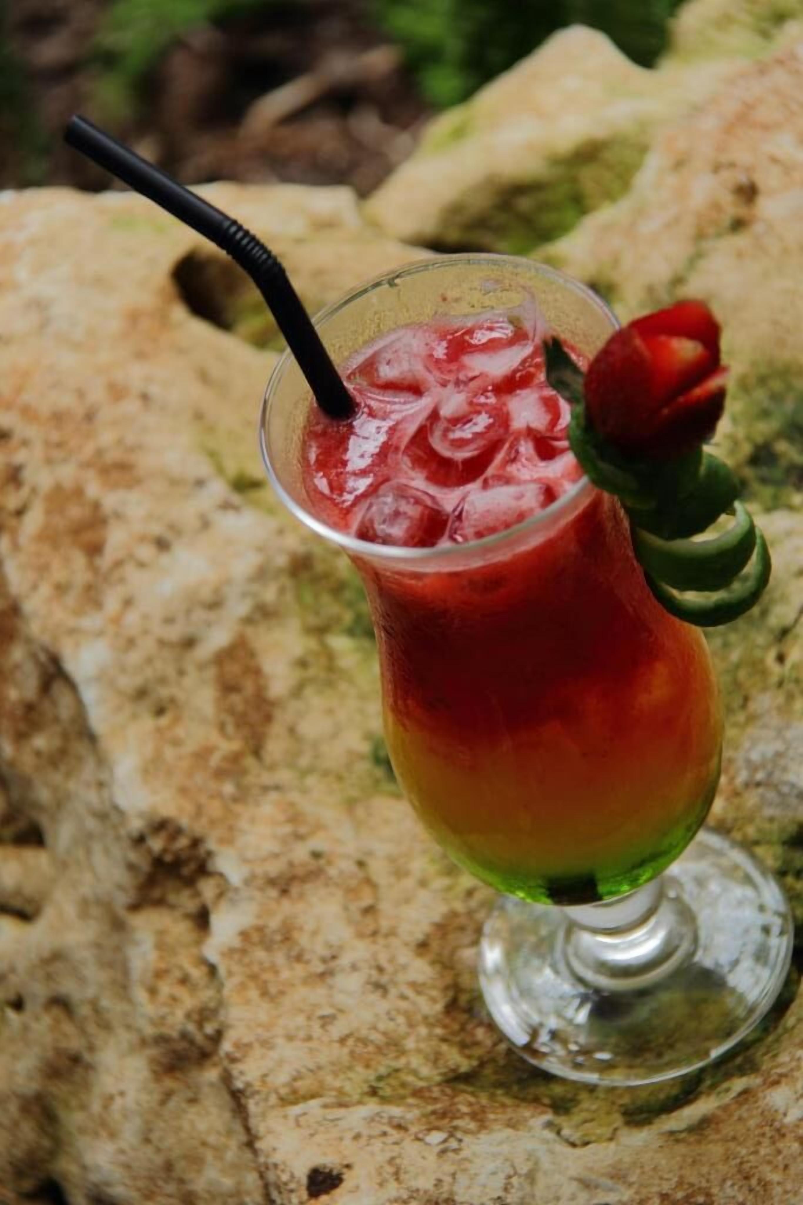 A cocktail in a glass with a rose garnish, placed on a stone surface.