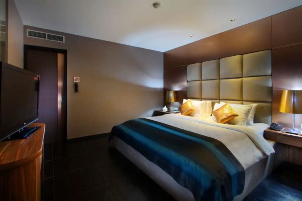 A hotel room with a large bed, a wooden desk, and a modern headboard.
