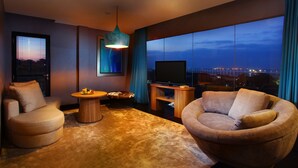 A modern living room with a large window, a flat-screen TV, and comfortable seating.