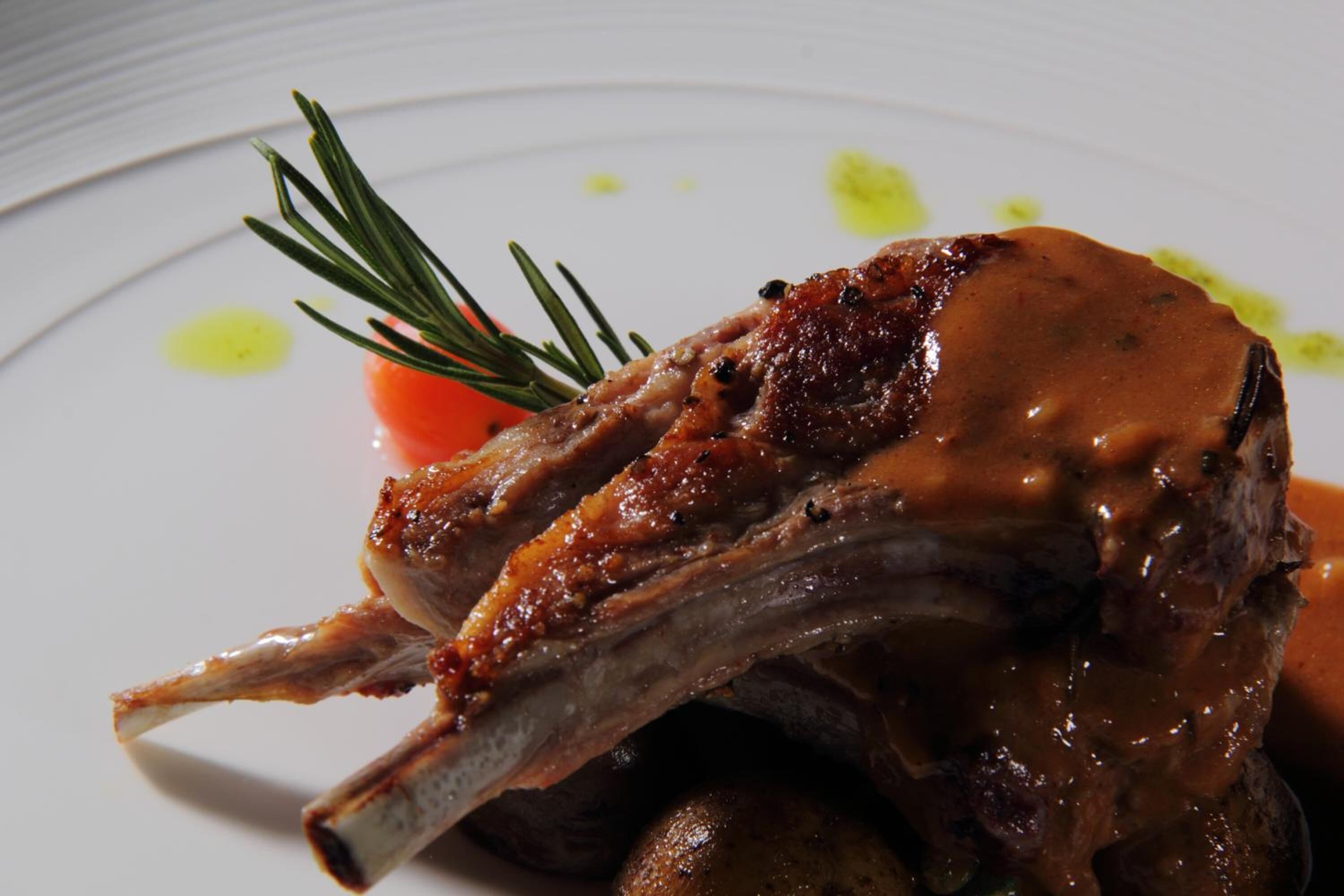 A plate with a cooked lamb chop, a sprig of rosemary, and some sauce.