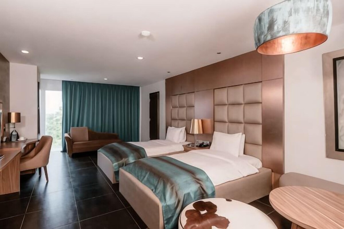 A hotel room with a large bed, a desk, a chair, a sofa, and a round table.