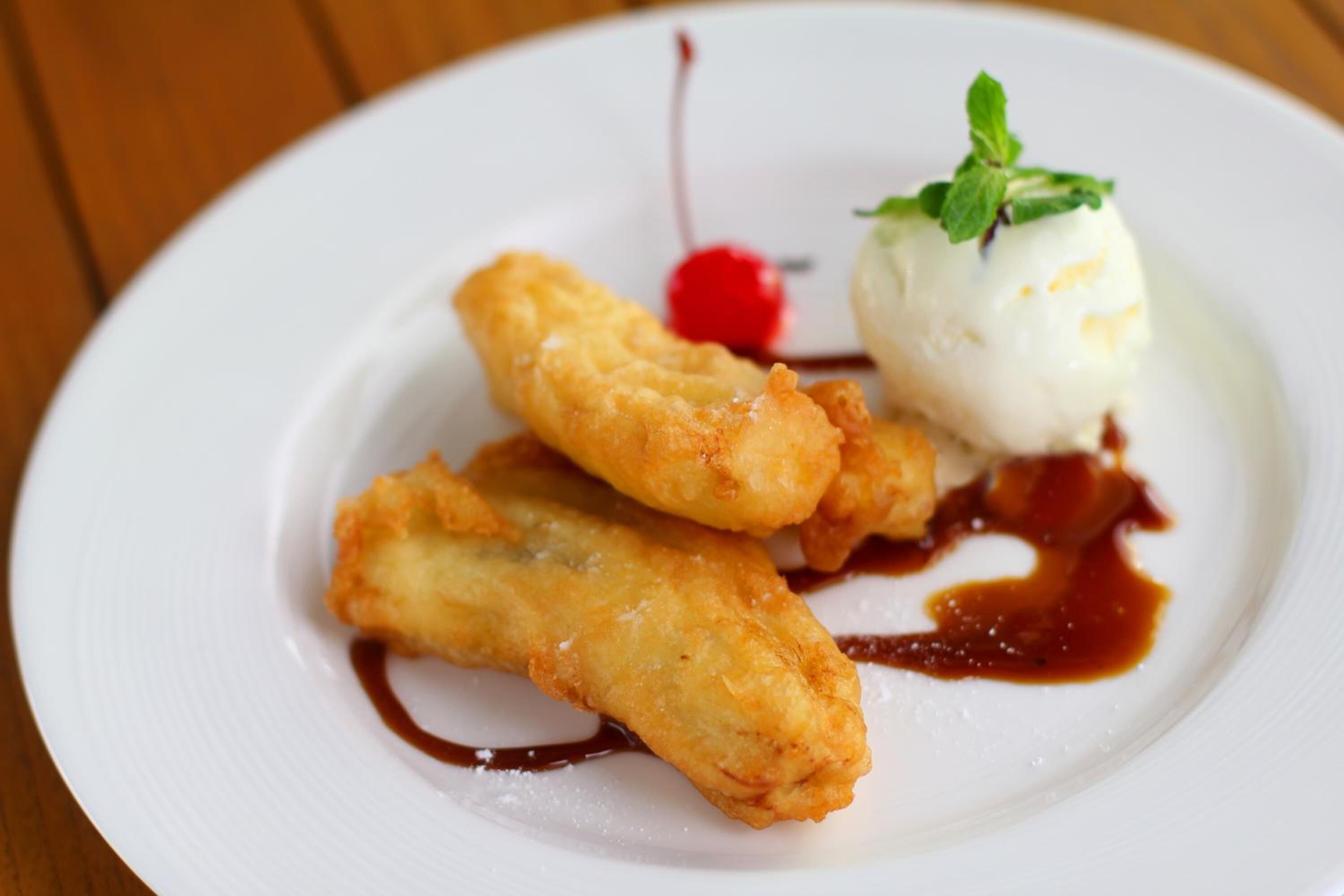 Une assiette de desserts comprenant des aliments frits, de la glace et une cerise.